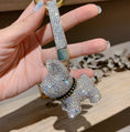 Charger l'image dans la visionneuse de la galerie, Hand holding white crystal dog keychain featuring gold keyring and sparkling wrist strap over a wooden surface
