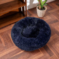 Load image into Gallery viewer, Navy blue plush round pet bed placed on wood floor next to a potted plant
