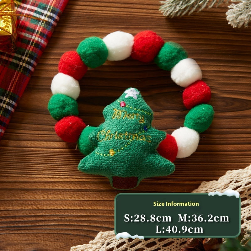 Close-up of a plush Christmas collar with red, green, and white felt balls and embroidered plush Christmas tree decoration on a wooden surface