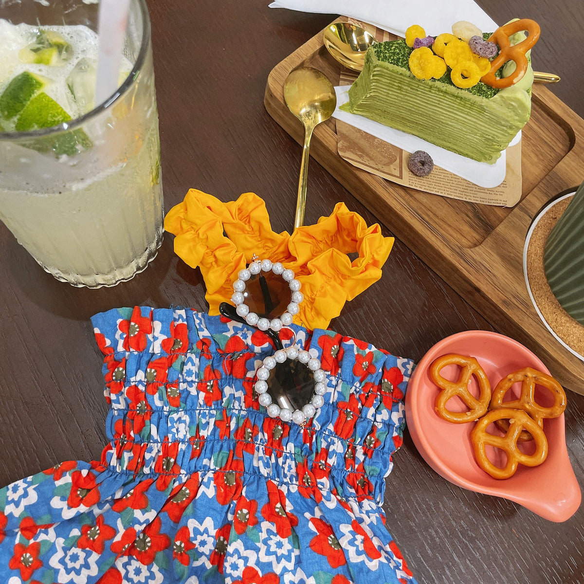 Pair of pearl frame round sunglasses on colorful dog dresses with drink and snacks on table