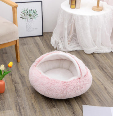 Pink plush dome pet bed on wooden floor near chair and small plant