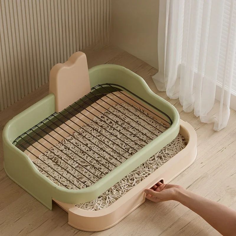 Green and peach indoor dog potty tray with metal grate and removable waste tray being pulled out by hand
