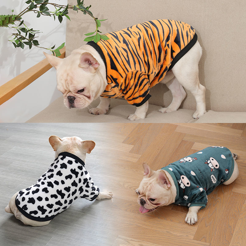 French bulldog dog wearing orange tiger-striped plush pajamas on beige couch