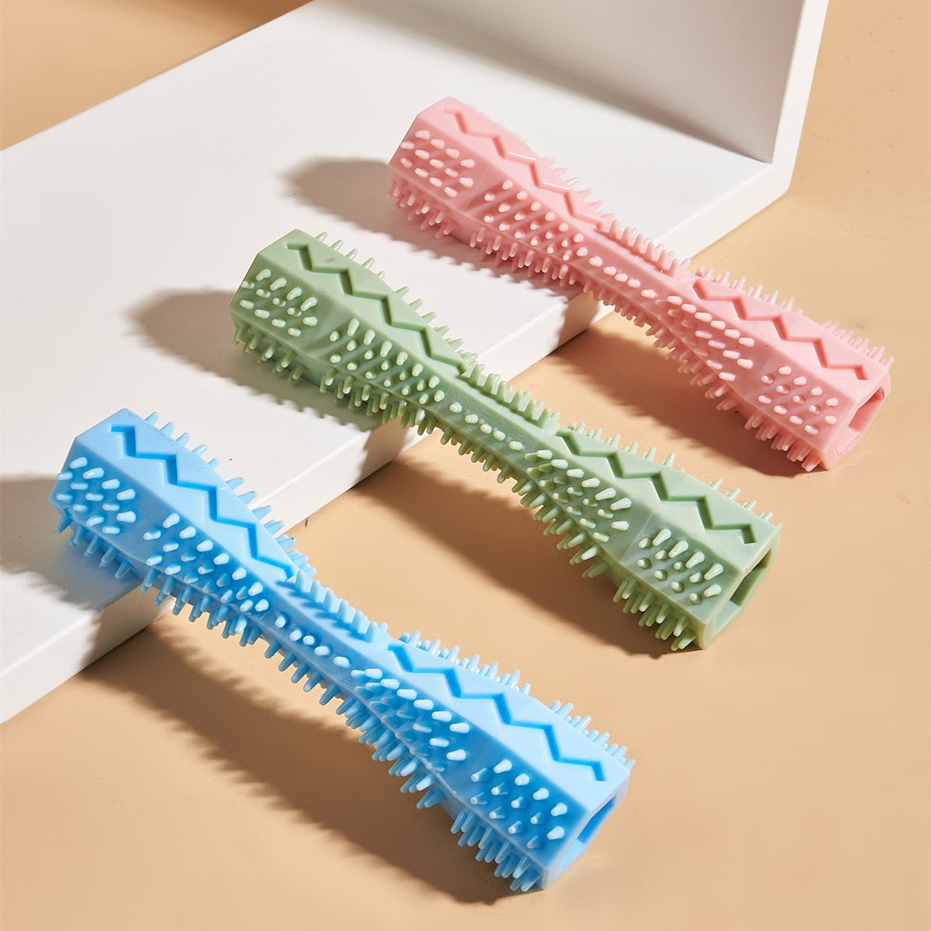 Close-up of pink, green, and blue rubber chew toys showing hollow interiors and textured bristles