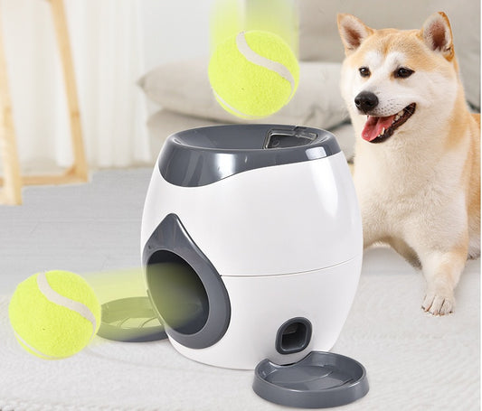White and gray interactive tennis ball pet feeder with tennis balls and a dog nearby