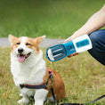 Load image into Gallery viewer, Smiling happy dog sitting outdoors next to person holding blue 3-in-1 portable dog water and food bottle
