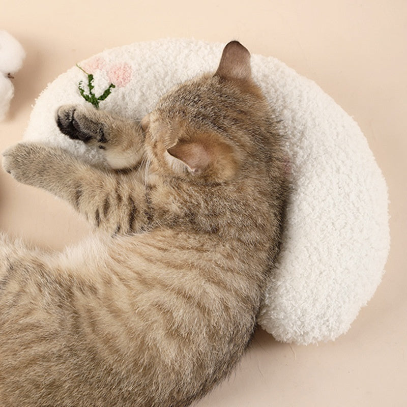 Kitten lying on white crescent-shaped plush pet pillow with pink flower embroidery
