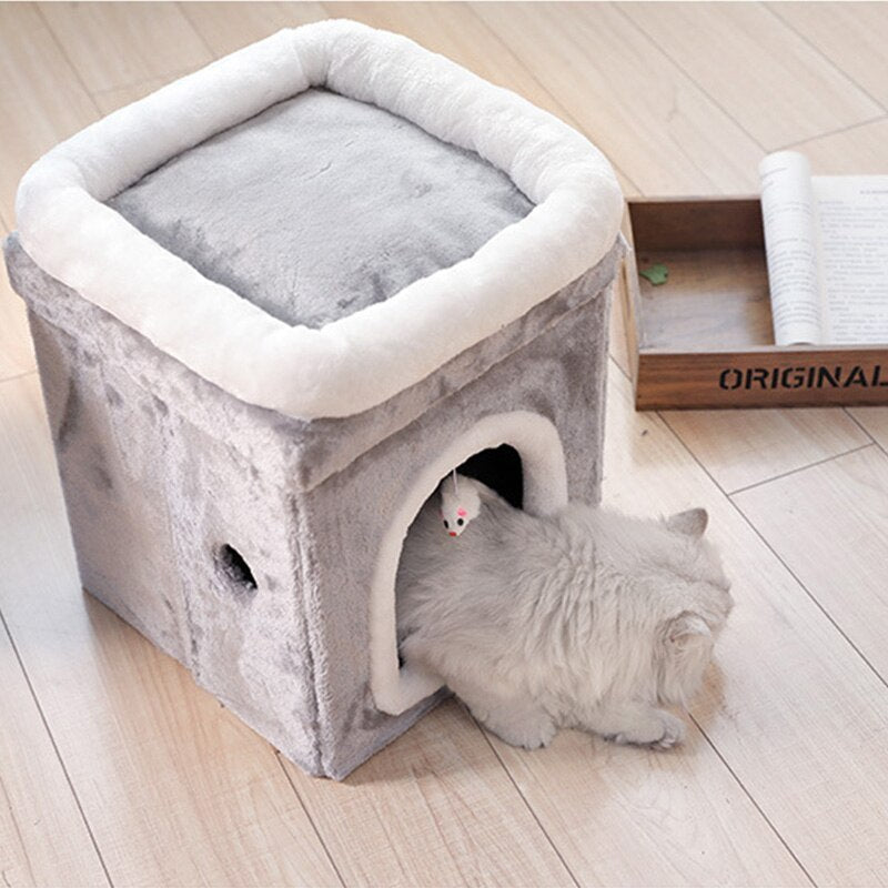 Cat entering the gray plush cat cave with white trim with a mouse toy hanging inside and a wooden tray nearby