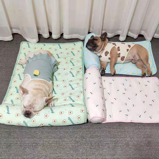 Two small dogs lying comfortably on pastel-colored cooling pet mats with attached pillows, one with avocado print and the other with a peach design