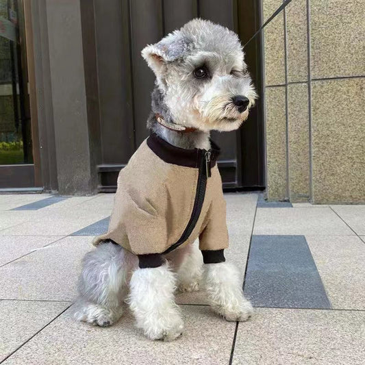 Small fluffy dog wearing khaki and black winter jacket sitting on tiled ground