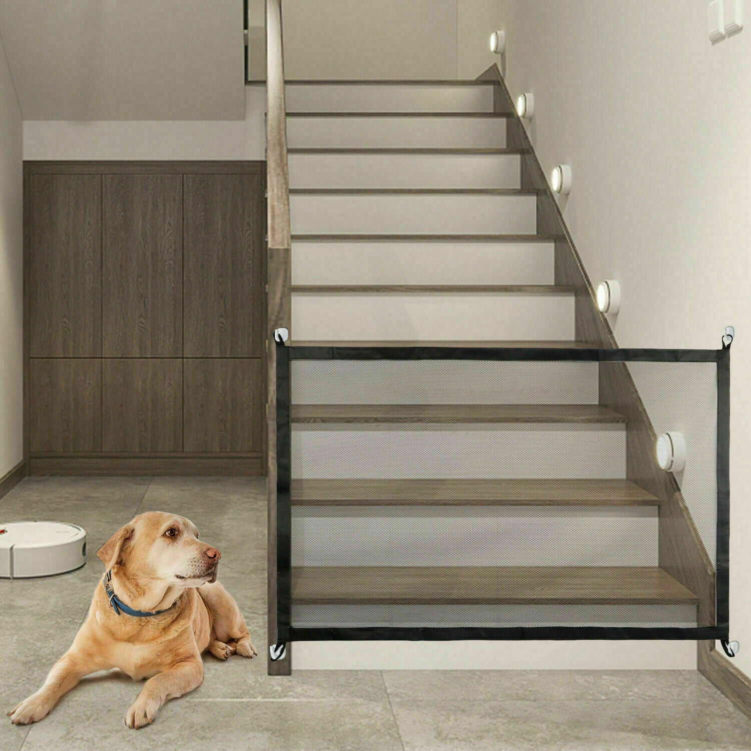 Portable black mesh safety gate installed at bottom of indoor wooden staircase with a dog lying nearby