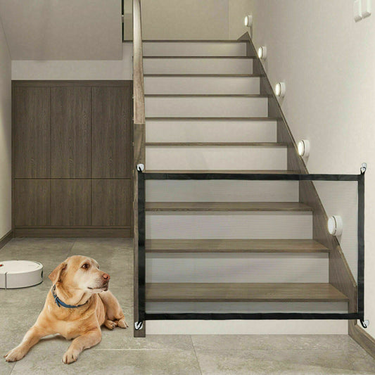 Portable black mesh safety gate installed at bottom of indoor wooden staircase with a dog lying nearby