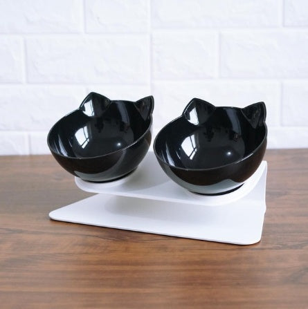 Black pair of cat ear bowls on elevated white stand photographed on wood