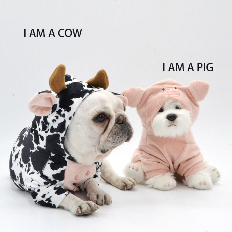 Two dogs dressed in animal costumes side-by-side on white background, one in a cow costume and the other in a pink pig costume with text: 'I AM A COW' and 'I AM A PIG'