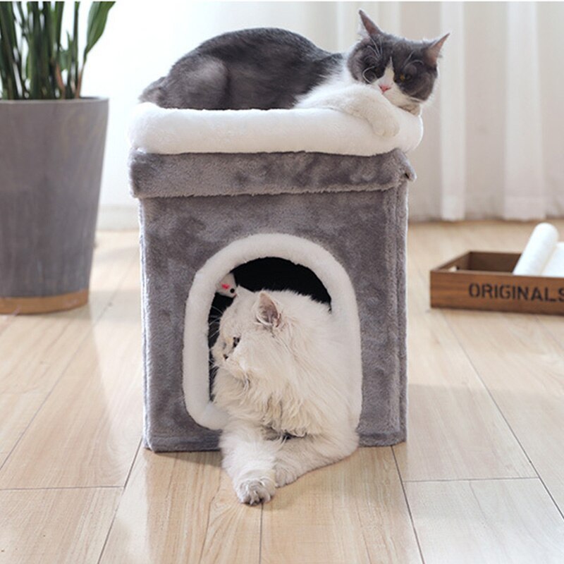 Gray and white cat lounging on top of the gray cat cave while a fluffy cat is inside looking out the entrance with mouse toy