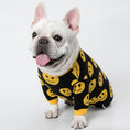Charger l'image dans la visionneuse de la galerie, White French Bulldog wearing black and yellow smiley face wool sweater sitting from side angle with tongue out
