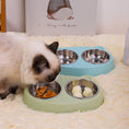 Load image into Gallery viewer, Cat eating treats from green double stainless steel bowls on a soft carpet with a blue set in background
