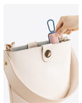 Load image into Gallery viewer, Hand placing the pink-blue bag dispenser inside a beige handbag
