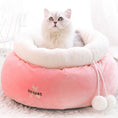 Load image into Gallery viewer, White fluffy cat sitting comfortably inside pink round plush cat bed with white fleece collar and pom-poms
