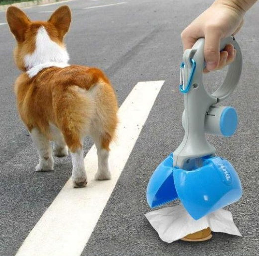 Corgi dog walking on a road with a person holding a blue and gray clamshell dog waste scooper picking up dog poop using disposable bag