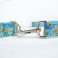 Load image into Gallery viewer, Close-up of silver metal clasp hooking onto metal D-ring of teal floral dog leash
