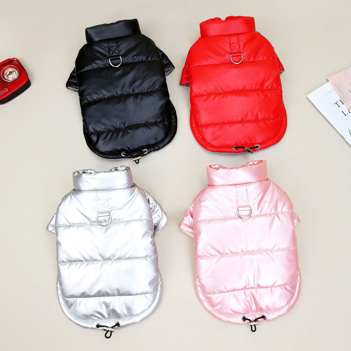 Four waterproof padded dog jackets displayed flat in black, red, silver, and pink colors with metal D-rings and adjustable drawstrings