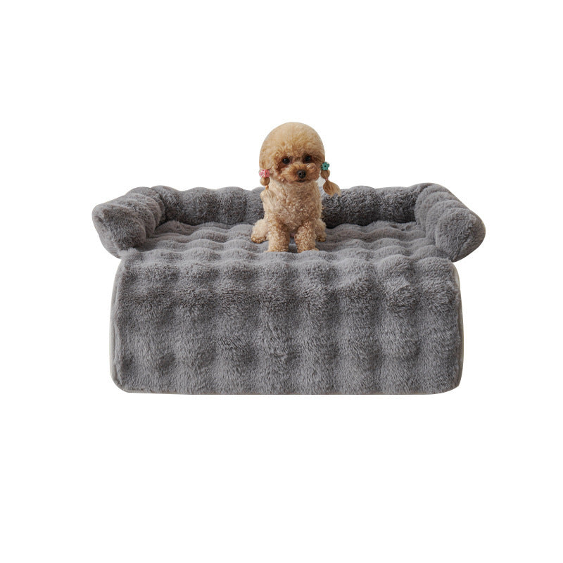 Small poodle sitting on gray plush dog mat with raised edges isolated on white background
