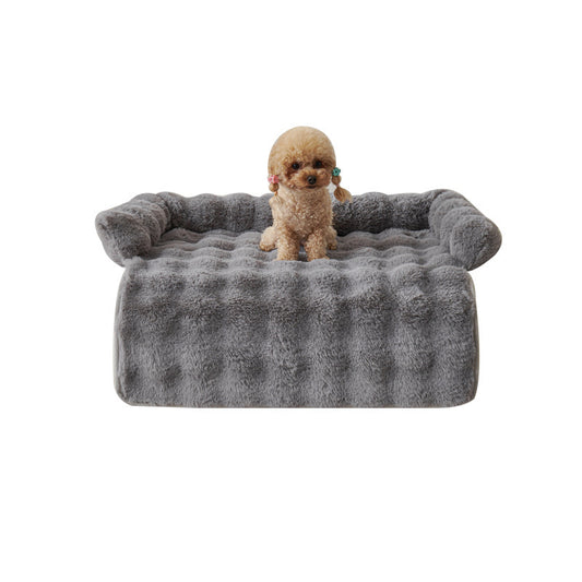 Small poodle sitting on gray plush dog mat with raised edges isolated on white background