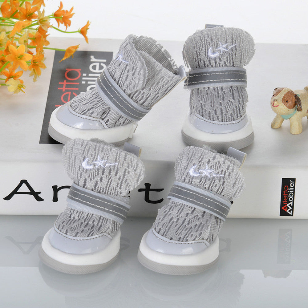 Set of gray knit dog booties with white soles and reflective strap on display surface