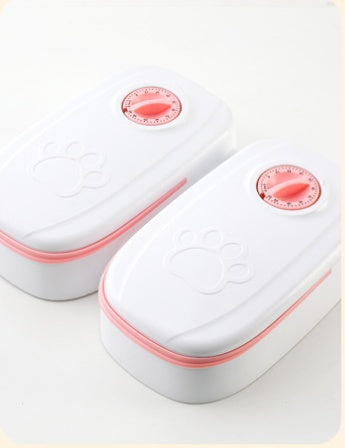 Two automatic pet feeders with white bodies and pink timer dials, lids closed, shown on white surface