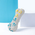 Load image into Gallery viewer, Bone-shaped dog chew toy with raised blue and yellow massage nodes standing upright on white surface next to blue mat
