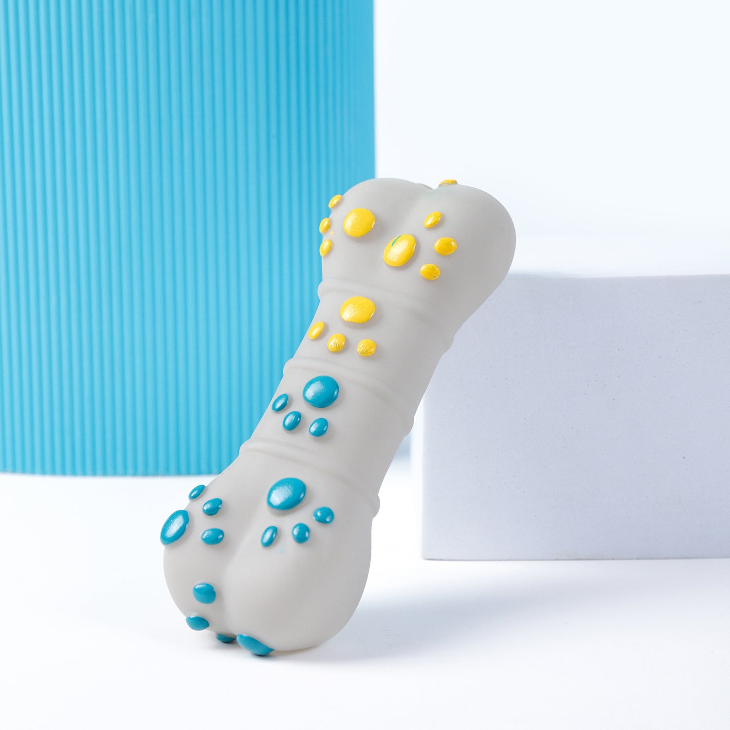 Bone-shaped dog chew toy with raised blue and yellow massage nodes standing upright on white surface next to blue mat