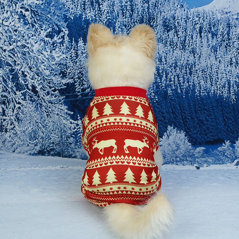 Small dog from behind wearing a red holiday pajama with cream Christmas tree and reindeer patterns against a winter snowy forest background