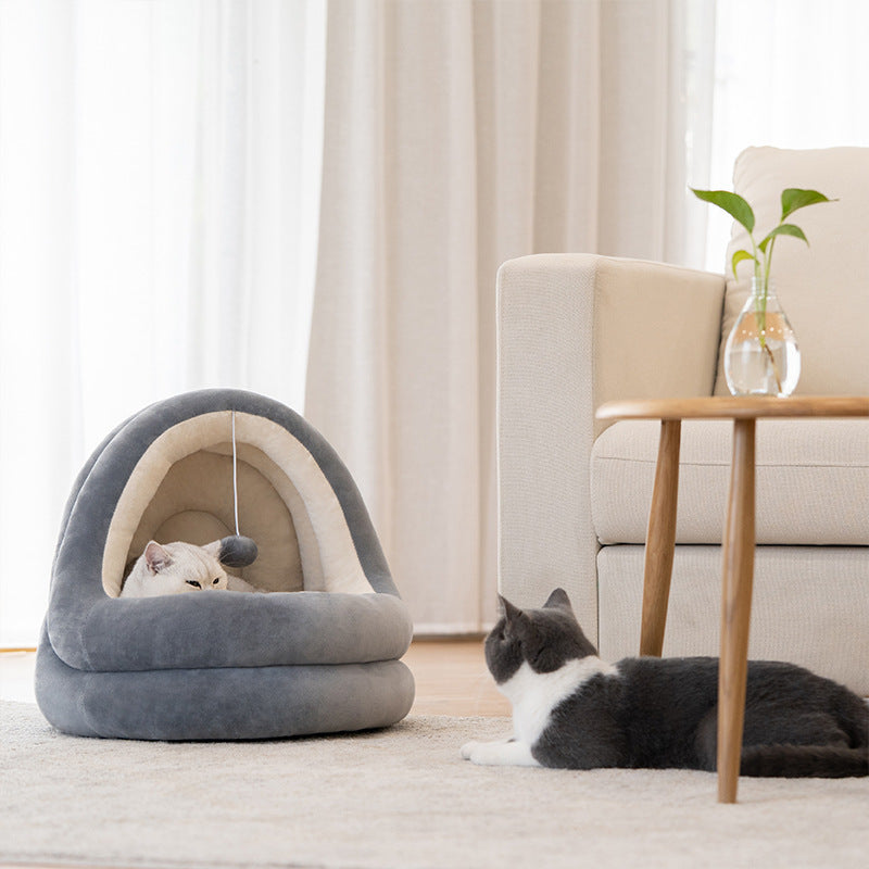 Gray plush pet cave bed placed on floor near sofa, with one cat inside bed and another cat nearby, highlighting the bed's cozy retreat design