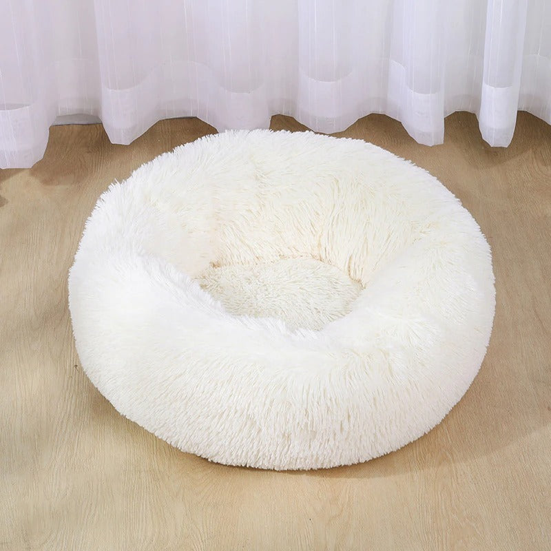 Cream-colored deep plush pet bed with thick fluffy sides placed on wooden floor