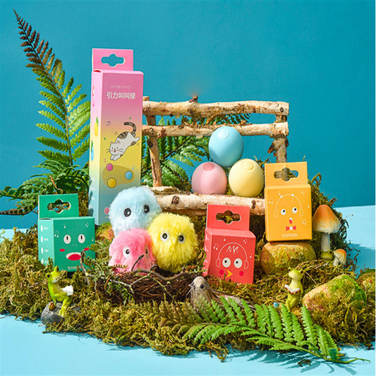 Colorful plush cat teaser balls and glowing plastic balls displayed with vibrant packaging amongst decorative moss and small figurines