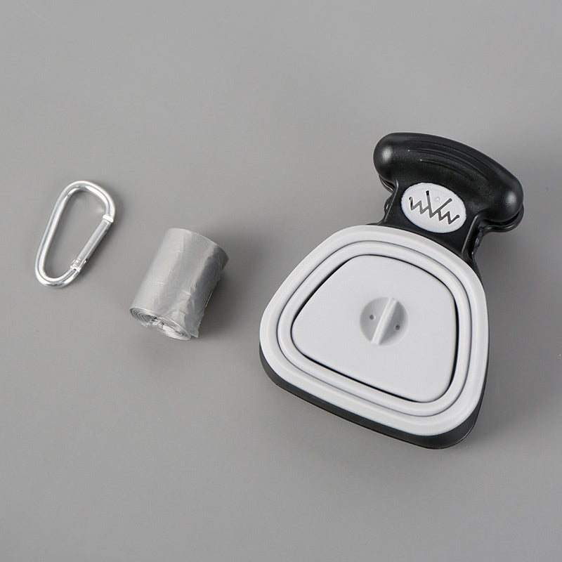 Foldable dog poop spoon dispenser with roll of plastic bags and metal carabiner on gray background