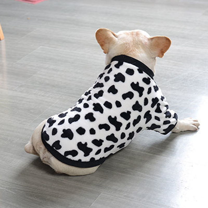 Dog wearing white and black spotted plush sweater lying on gray floor