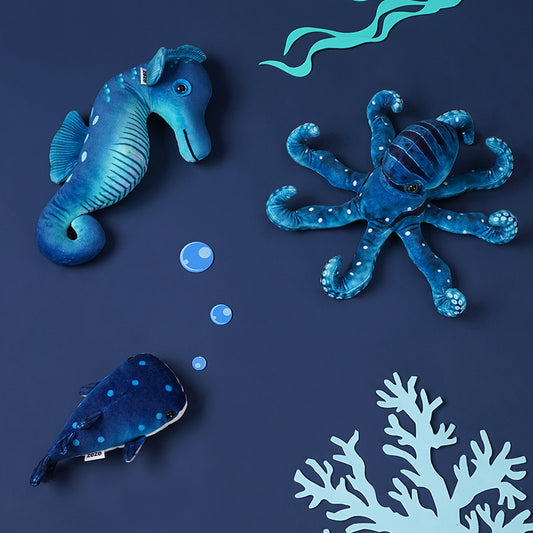 Blue ocean-themed plush toys including seahorse, octopus, and whale arranged on a dark blue surface with bubble and coral decorations