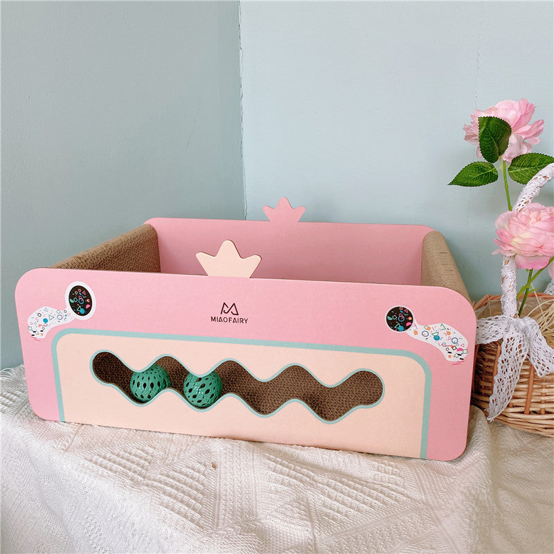 Empty pink corrugated cat scratcher bed with heart-shaped cutouts and green balls on table