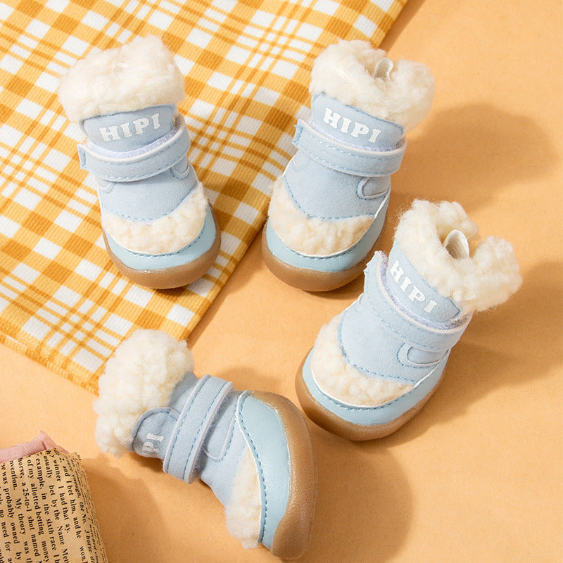 Two light blue fleece-lined dog booties with rubber soles positioned on yellow plaid fabric