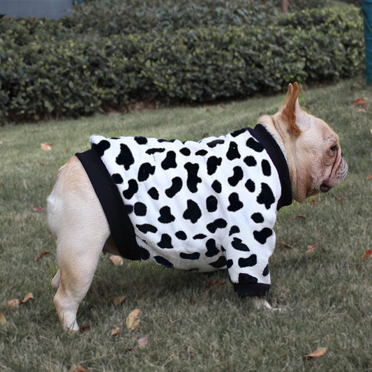Side view of French Bulldog wearing white fleece dog sweater with black spots resembling cow print standing on grass