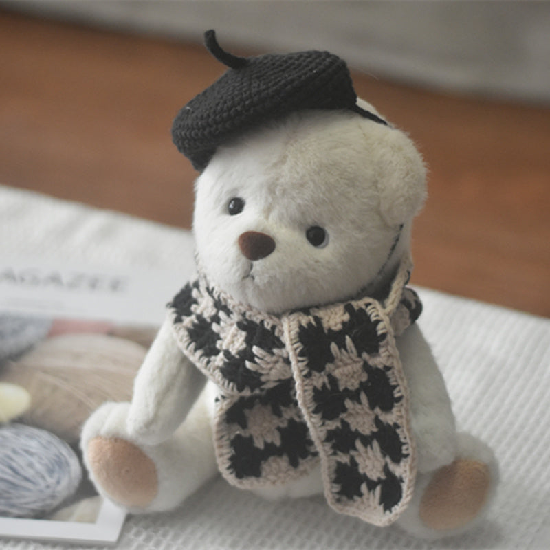 White teddy bear plush toy wearing a black knitted beret and black-beige plaid scarf