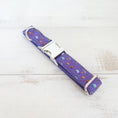 Load image into Gallery viewer, Laid flat purple Halloween dog collar featuring metal buckle and D-ring on light wood surface
