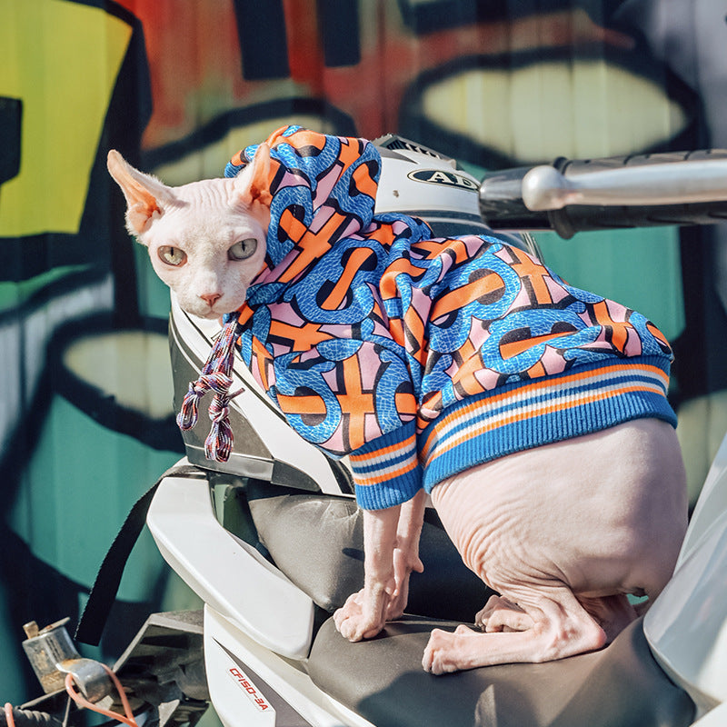 Hairless cat perched on scooter wearing vibrant graphic hoodie with hood up