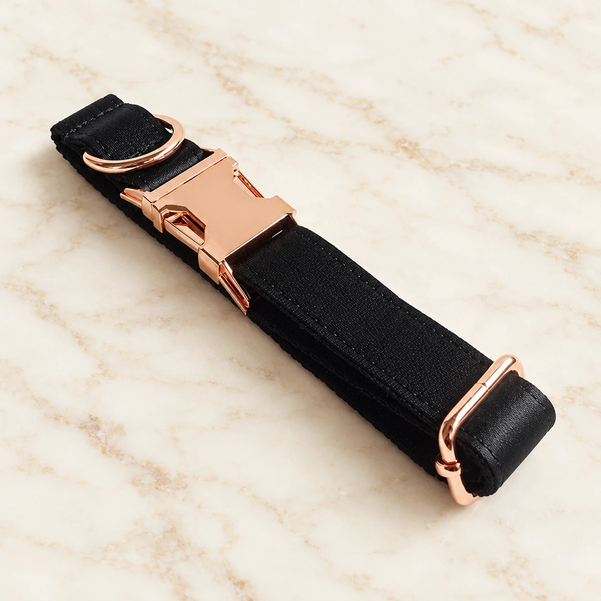 Folded black collar showing the rose-gold-tone buckle, D-ring and adjustment slider