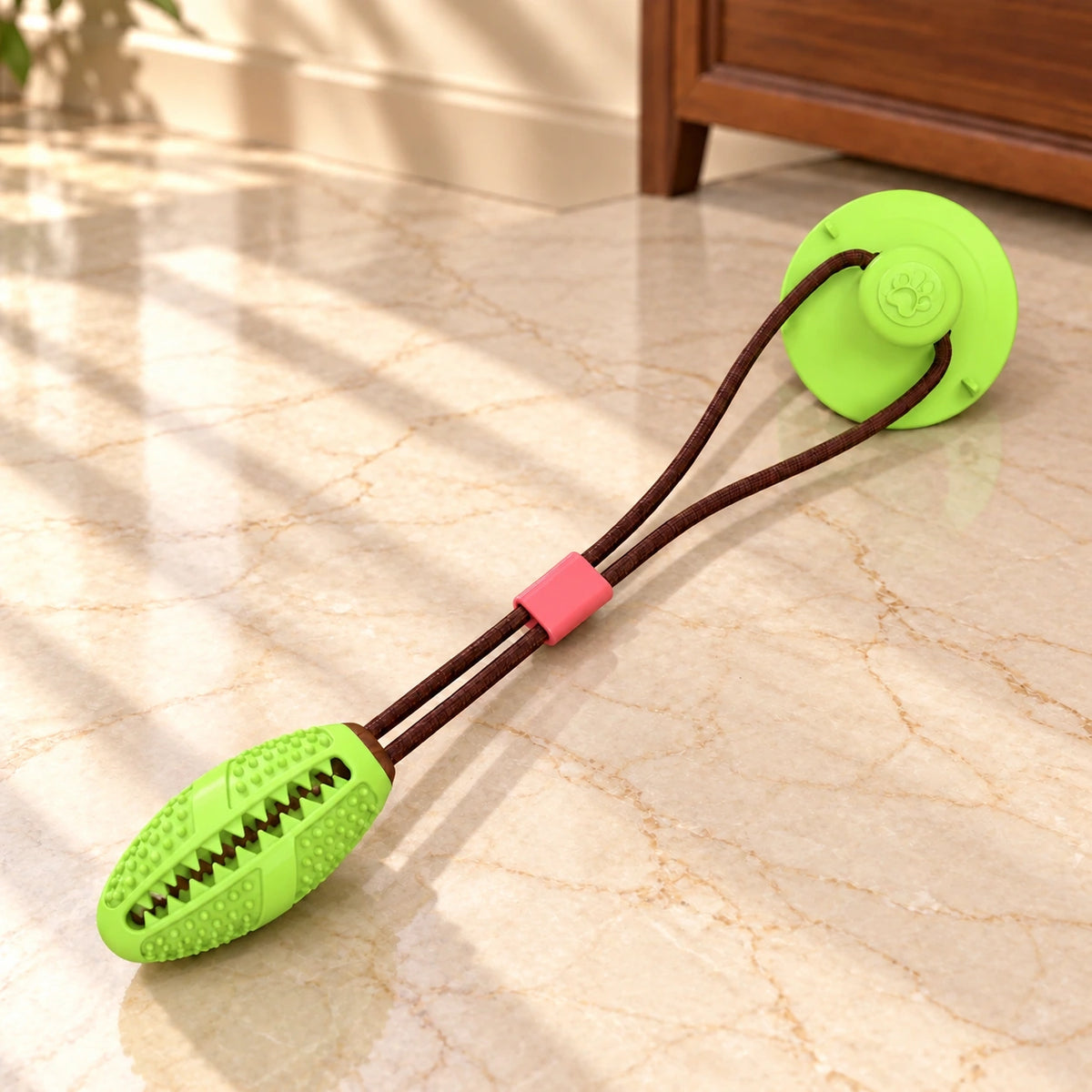 Lime green oval dog tug toy with brown cord and suction cup on light ivory-beige marble