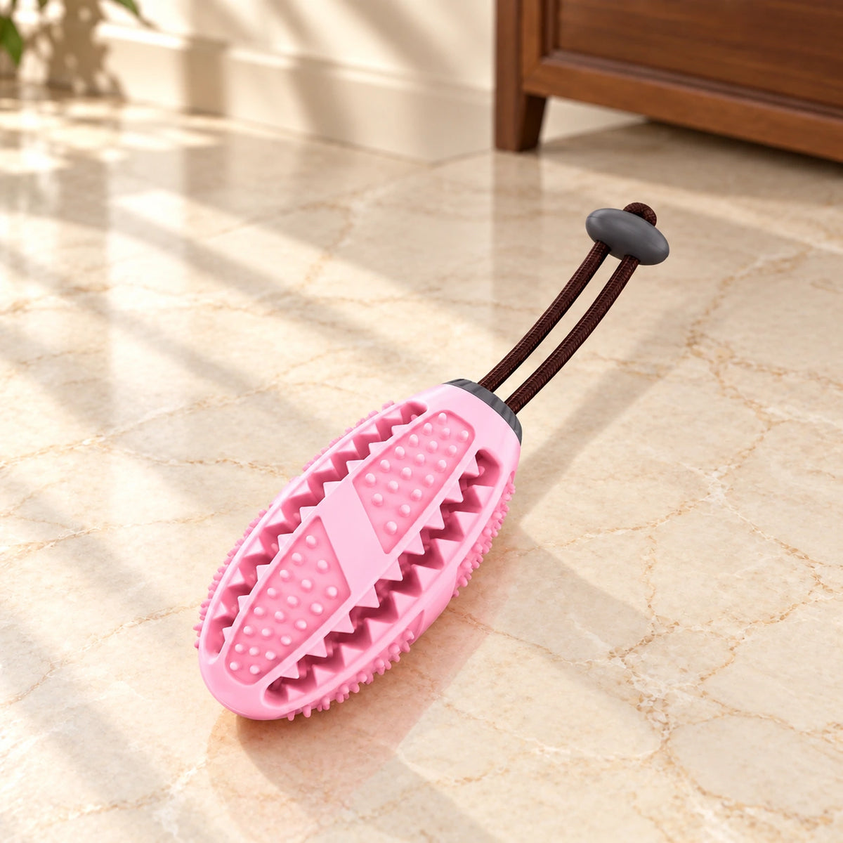 Pink oval dog chew toy with short dark pullcord on light ivory-beige marble
