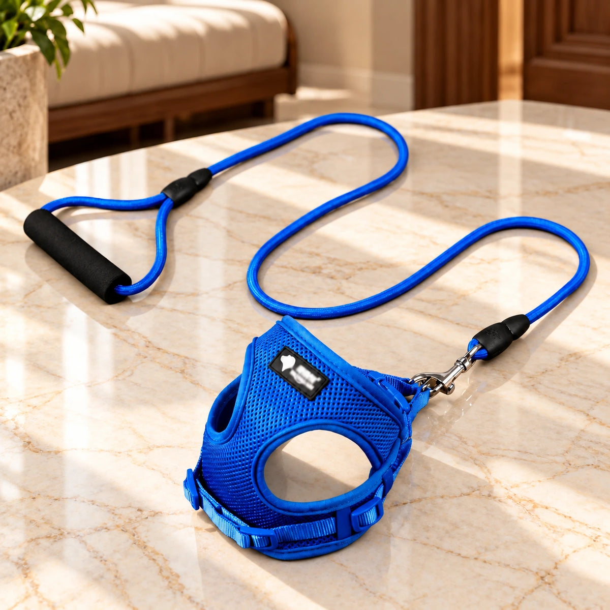 Blue mesh dog harness and matching rope leash with a black foam handle on light ivory-beige marble.