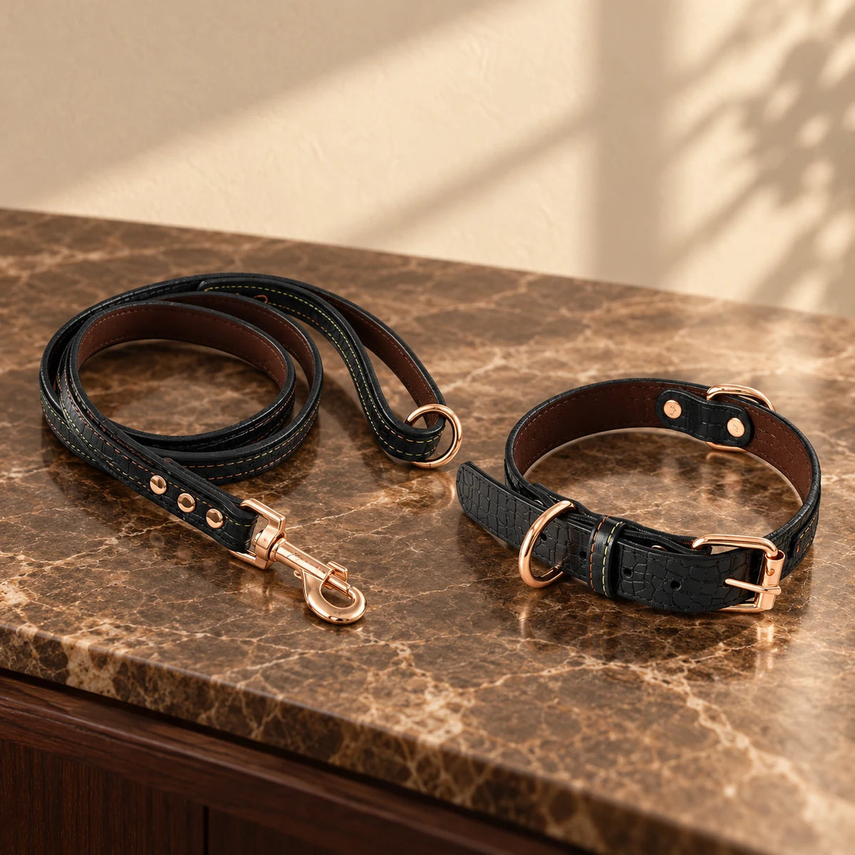 Black croc-texture dog collar and matching leash with rose-gold hardware on brown marble.